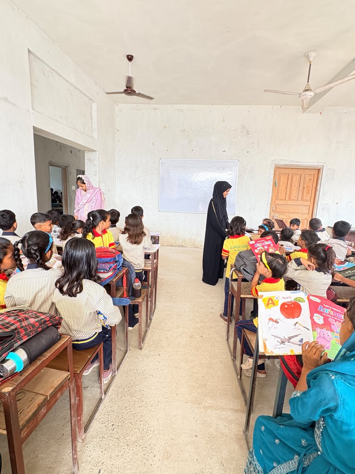 A teacher guiding young students with their books
